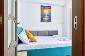 Une chambre à coucher avec un lit, des oreillers, un tableau accroché au mur et une porte.