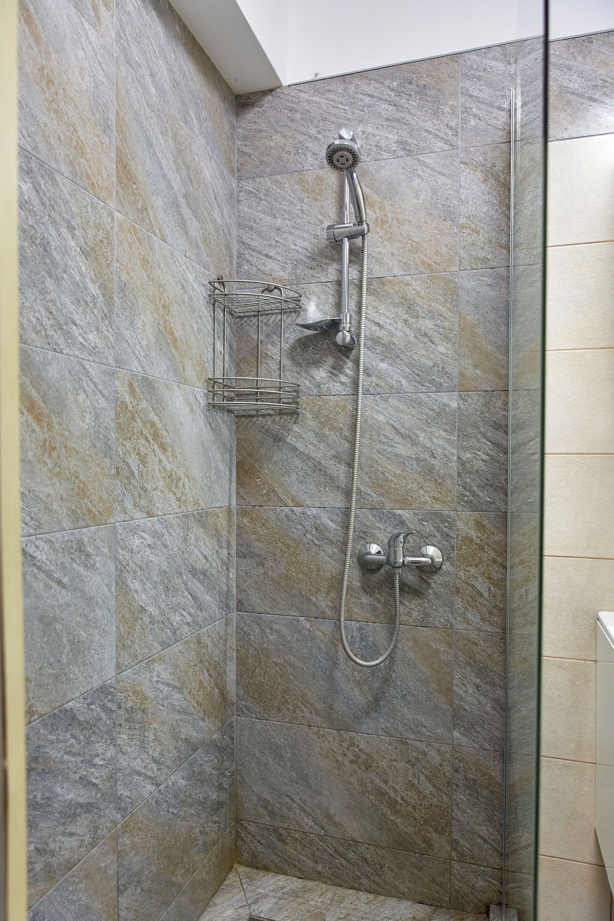 A shower area with a glass partition, a handheld showerhead, and a wall-mounted faucet.