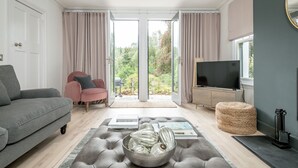 A modern living room with a grey sofa, a pink chair, a television, and a large window with curtains.