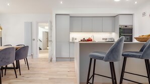 A modern kitchen with grey cabinets, a central island with bar stools, and a dining area with a wooden table and grey chairs.