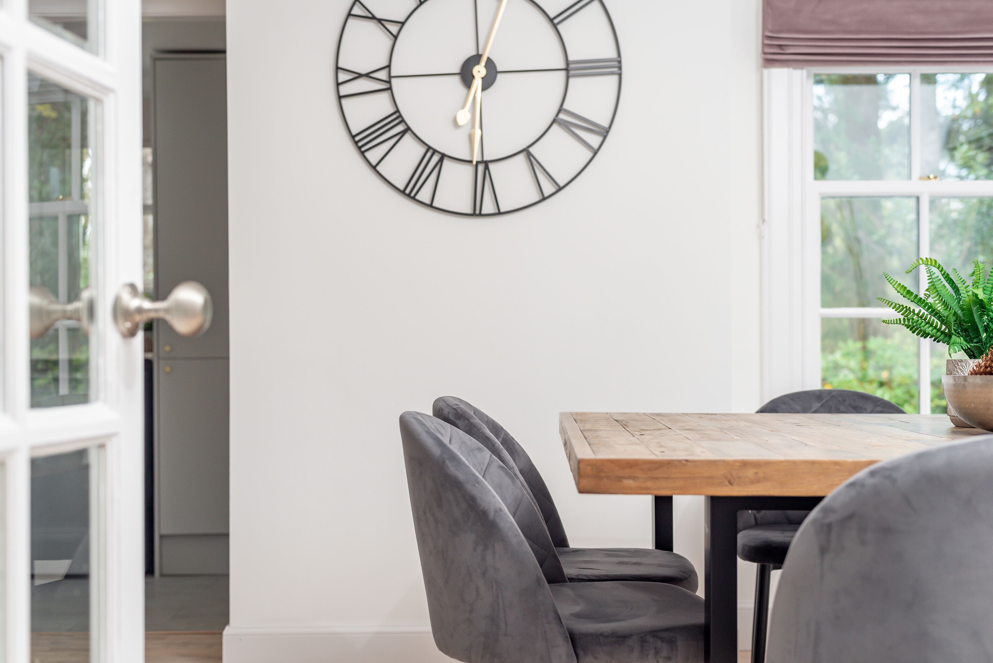 A dining area with a wooden table, grey upholstered chairs, and a wall-mounted clock.