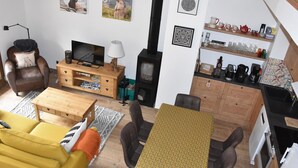 Una sala de estar acogedora con sofá, mesa de centro, televisor, chimenea y zona de cocina con estantes y electrodomésticos.
