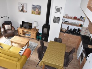 Ein gemütliches Wohnzimmer mit Sofa, Couchtisch, Fernseher, Kamin und Küchenbereich mit Regalen und Geräten.