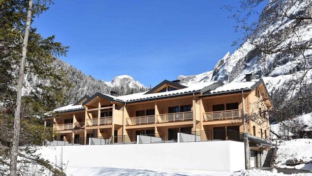 Una cabaña de madera de varios pisos con balcones, con el paisaje de una montaña nevada al fondo.