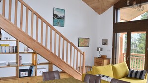 Una sala de estar acogedora con una escalera de madera, un sofá amarillo, una mesa de comedor y una estantería.