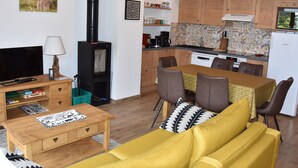 Una sala de estar acogedora con un sofá, televisión y chimenea. Hay un comedor con una mesa y sillas. La cocina tiene armarios de madera y un salpicadero de azulejos.