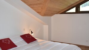 Un dormitorio con techo de madera, paredes blancas y una cama grande con almohadas rojas.