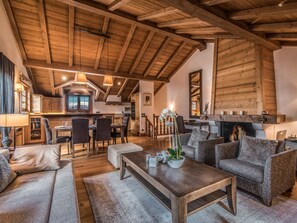 A spacious living area with a high wooden ceiling, a fireplace, and a dining area with a view of the mountains.