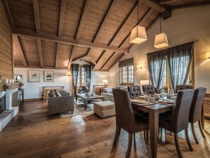 Ampla sala de estar com teto alto de madeira, mesa de jantar posta para quatro e um espaço de estar acolhedor.