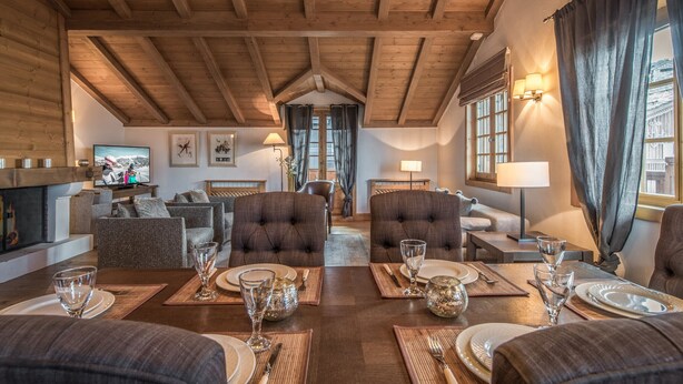 Un ampio soggiorno con soffitto in legno a volta, un camino e un'area pranzo apparecchiata per un pasto.