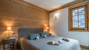 Camera da letto con soffitto in legno, un letto con copripiumino grigio, due abat-jour, un comodino e una finestra vista edifici.