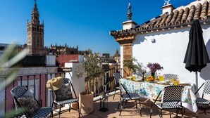 Une terrasse avec des sièges extérieurs, une table dressée avec des boissons et une vue sur une tour historique.