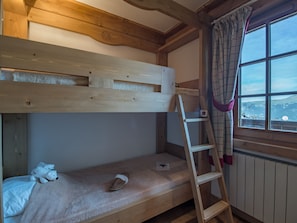 A bunk bed with a ladder, a window with a view, and a teddy bear on the lower bunk.