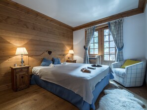 Ein Schlafzimmer mit Holzwandverkleidung, einem Bett, zwei Nachttischen, einem Sessel und einem Fenster mit Vorhängen.