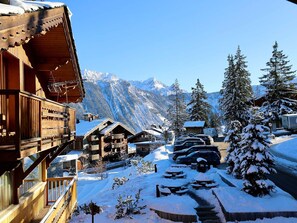 Eine Holzhütte mit Balkonen, einer verschneiten Auffahrt und einem Berg im Hintergrund.
