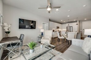 A modern living room with a glass coffee table, a white sofa, and a dining area with a white chair.
