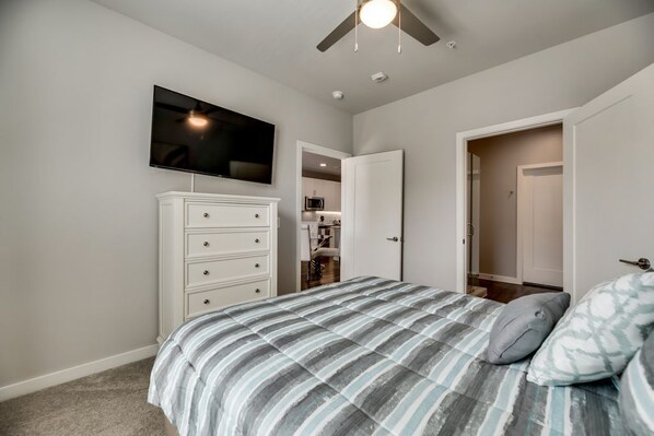 A bedroom with a bed, a TV mounted on the wall, a ceiling fan, and a wardrobe.