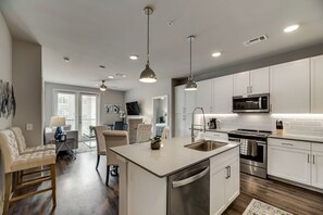 A modern kitchen with white cabinets, stainless steel appliances, and pendant lighting.