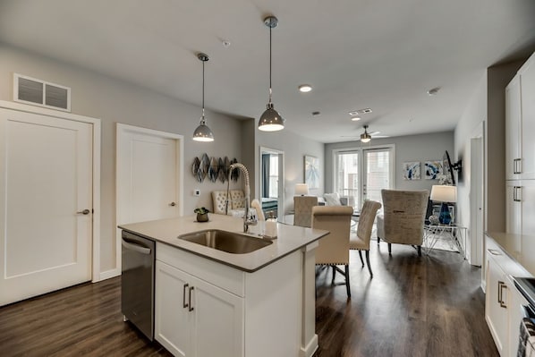 A modern kitchen with a central island, pendant lighting, and a dining area with a chair and table.