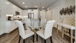 A modern kitchen with white cabinetry, a glass dining table, and pendant lighting. - MCK203 - Apt|Patio|15mi to Toyota Stadium|Sleeps 4 (McKinney)