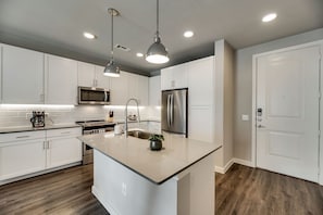 A modern kitchen with white cabinetry, stainless steel appliances, and pendant lighting.