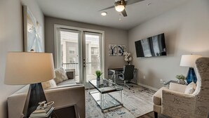 A modern living room with a glass coffee table, a sofa, a chair, and a ceiling fan. - MCK203 - Apt|Patio|15mi to Toyota Stadium|Sleeps 4 (McKinney)