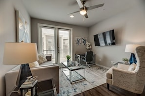 A modern living room with a glass coffee table, a sofa, a chair, and a ceiling fan. - MCK203 - Apt|Patio|15mi to Toyota Stadium|Sleeps 4 (McKinney)