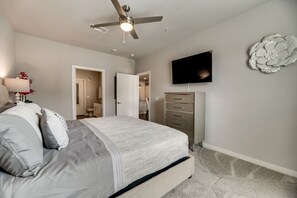 Ein Schlafzimmer mit Bett, Deckenventilator, Fernseher, Kommode und einer Wanddekoration.