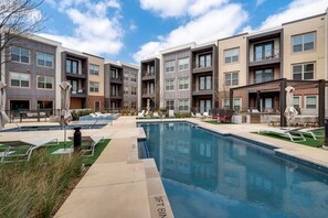 A residential building with a swimming pool, outdoor seating, and a clear sky.