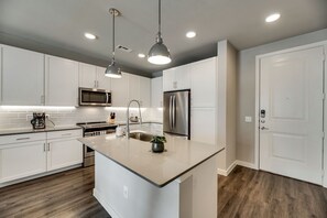A modern kitchen with white cabinetry, stainless steel appliances, and pendant lighting.