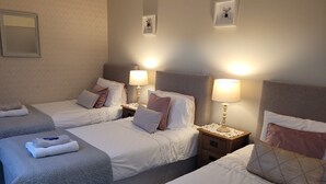 Une chambre d’hôtel avec trois lits, chacun étant muni d’une table de chevet et d’une lampe.