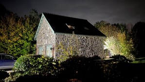 Un bâtiment en pierre doté d’un toit à forte pente, entouré d’un feuillage dense.