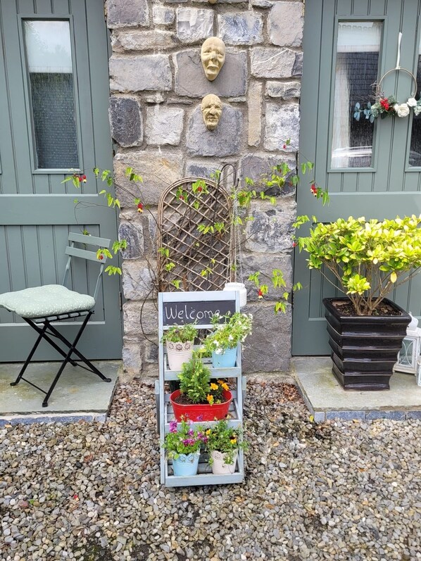 A stone wall with a welcome sign, a metal trellis, and a variety of potted plants. - An Irish welcome. Quiet Country Cottage close to Dublin Airport & City (Ashbourne)