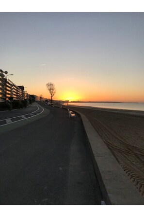 Stroll along the serene coastal road, lined with a sandy beach and a sidewalk, perfect for a peaceful walk.