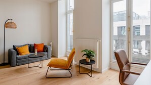 Een moderne woonkamer met een grijze bank, een gele fauteuil, een klein rond tafeltje en een vloerlamp.