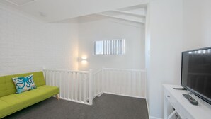 A room with a green sofa, a white wall, a white railing, a TV, and a remote control. - Moondance 2 - Canal front duplex (Yamba)