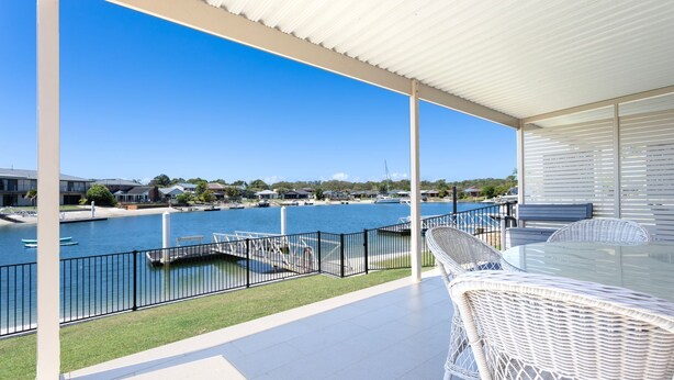 A covered outdoor area with a view of a marina and boats, featuring a glass table and wicker chairs. - Moondance 2 - Canal front duplex (Yamba)