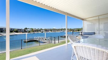 A covered outdoor area with a view of a marina and boats, featuring a glass table and wicker chairs.