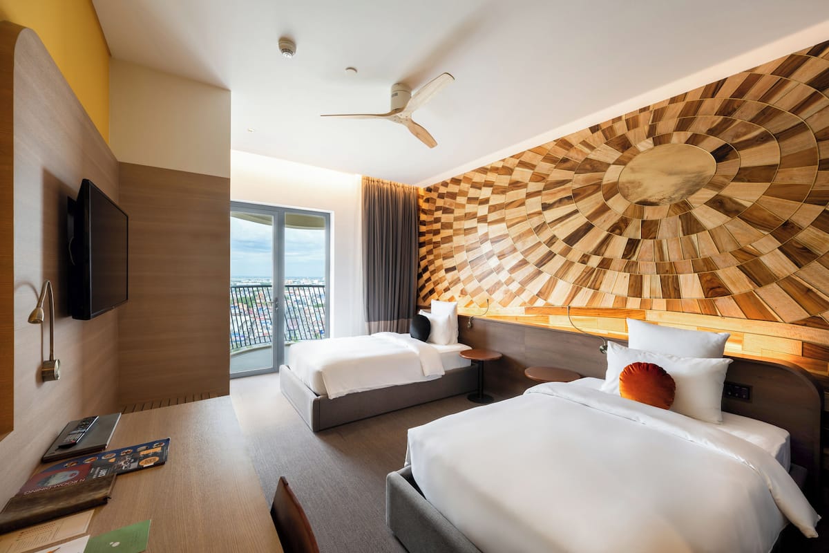 A hotel room with two beds, a desk with a laptop, a TV, and a ceiling fan.
