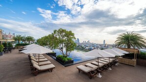 A rooftop pool area with lounge chairs and umbrellas, overlooking a cityscape. - SUN & MOON, Riverside Hotel (Phnom Penh)