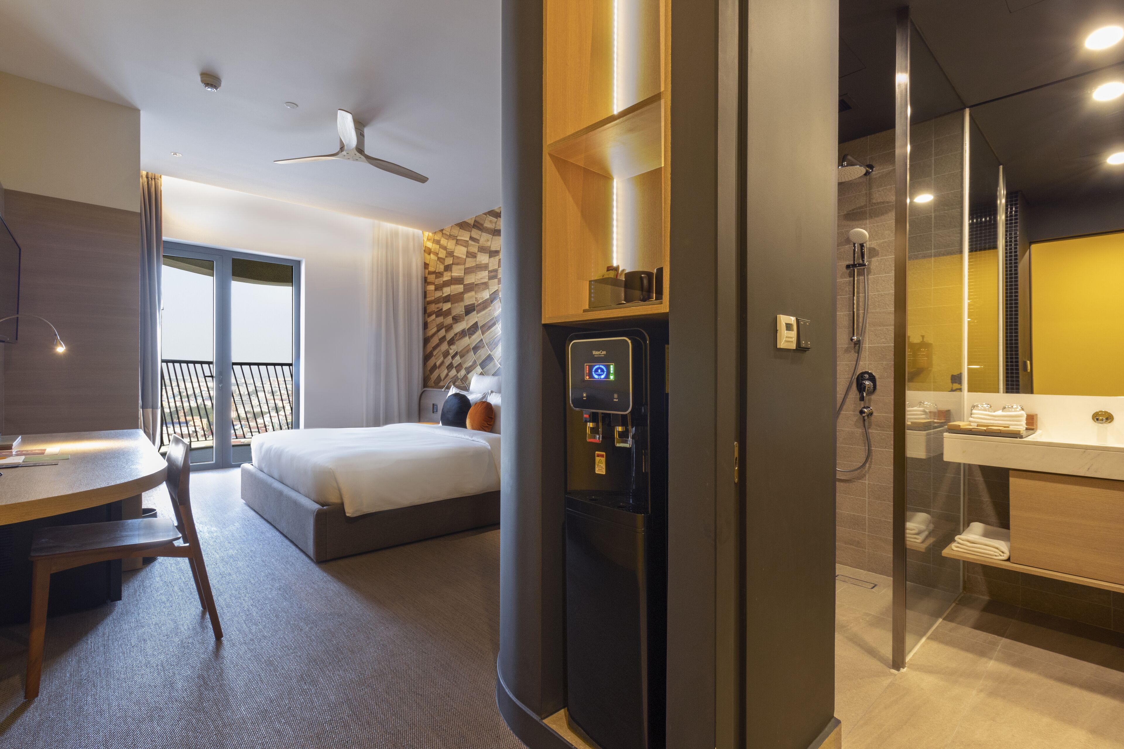Ein Hotelzimmer mit Bett, Schreibtisch, Stuhl, Minibar, Duschbereich und einem Badezimmer mit Spiegel.