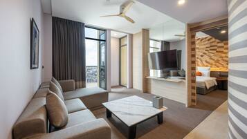 A modern hotel room with a sofa, a coffee table, a TV, and a balcony with curtains.