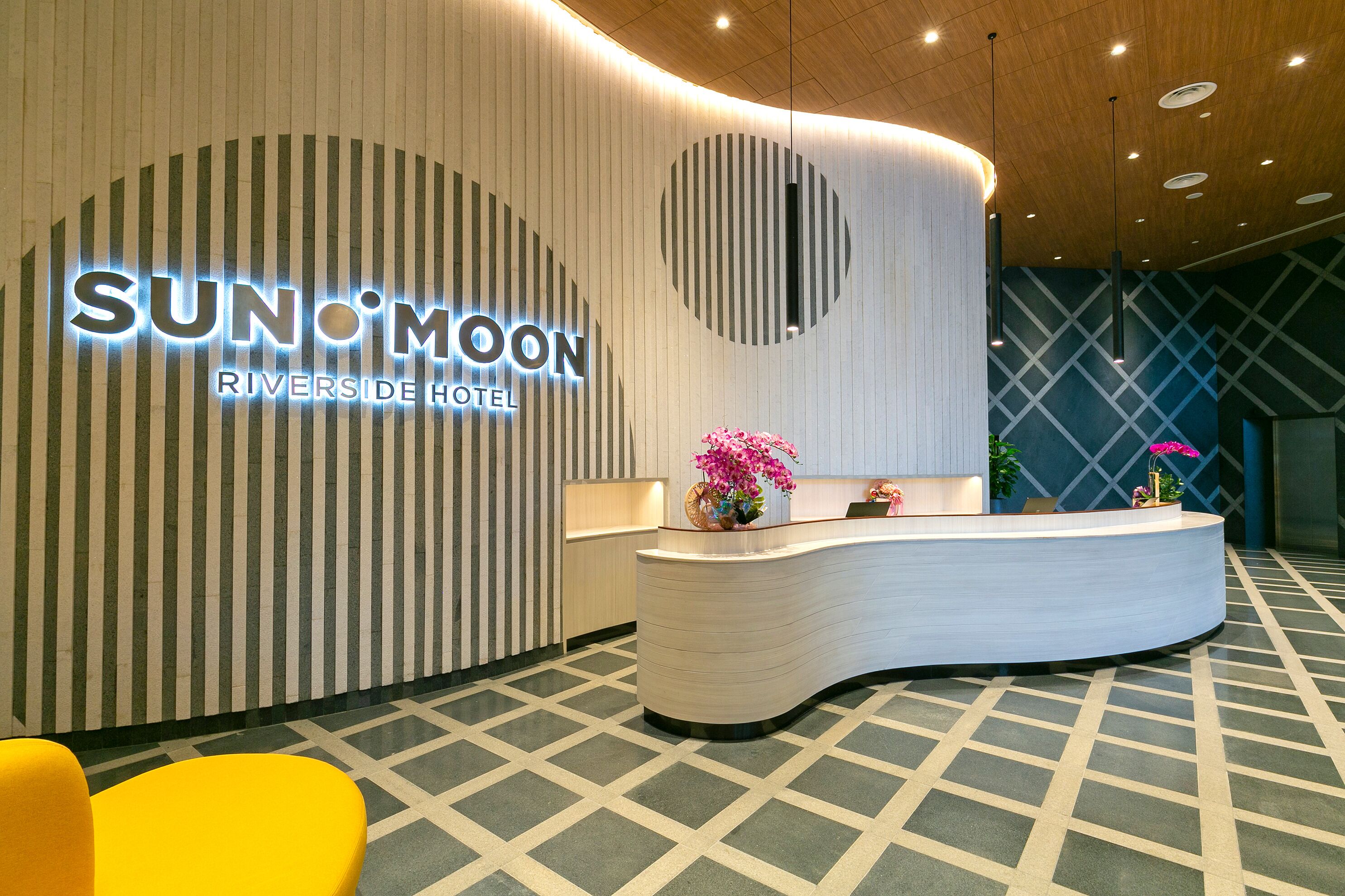 A hotel reception area with a modern design, featuring a curved reception desk, a large illuminated sign, and a patterned floor.