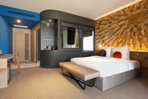 Een moderne hotelkamer met een gebogen muur, een groot bed, een bankje en een uniek houten plafondontwerp.