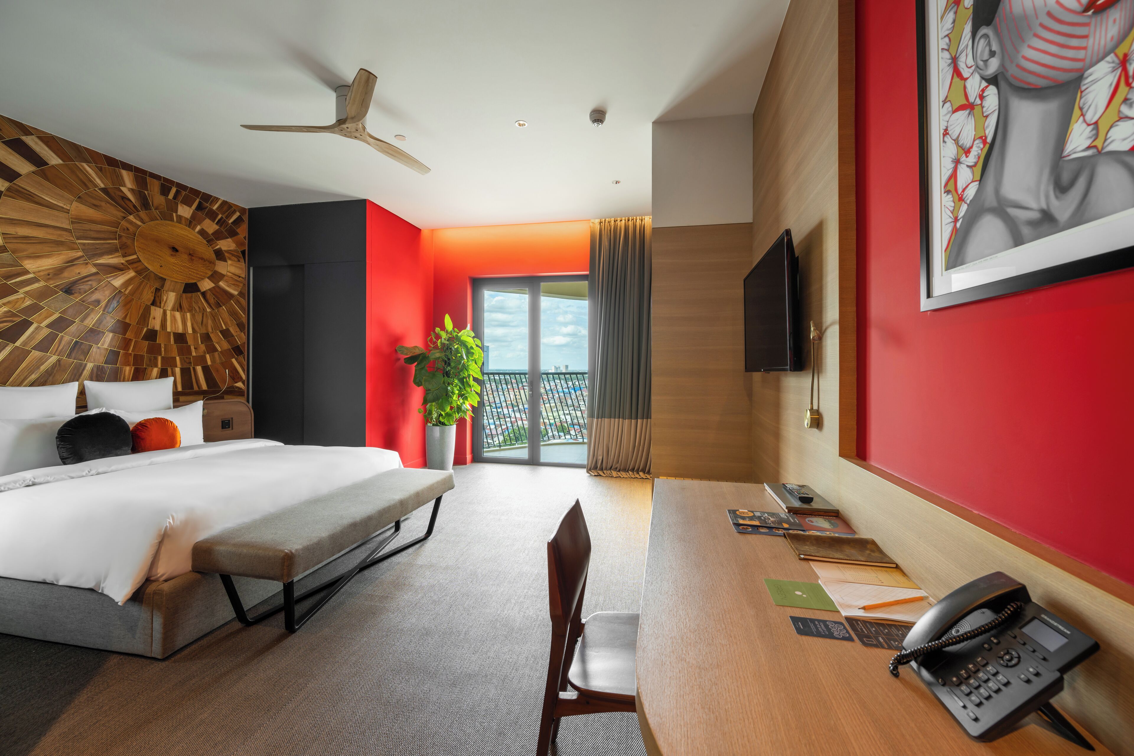 A hotel room with a bed, a desk, a chair, a telephone, a television, and a large window with a view of the outside.