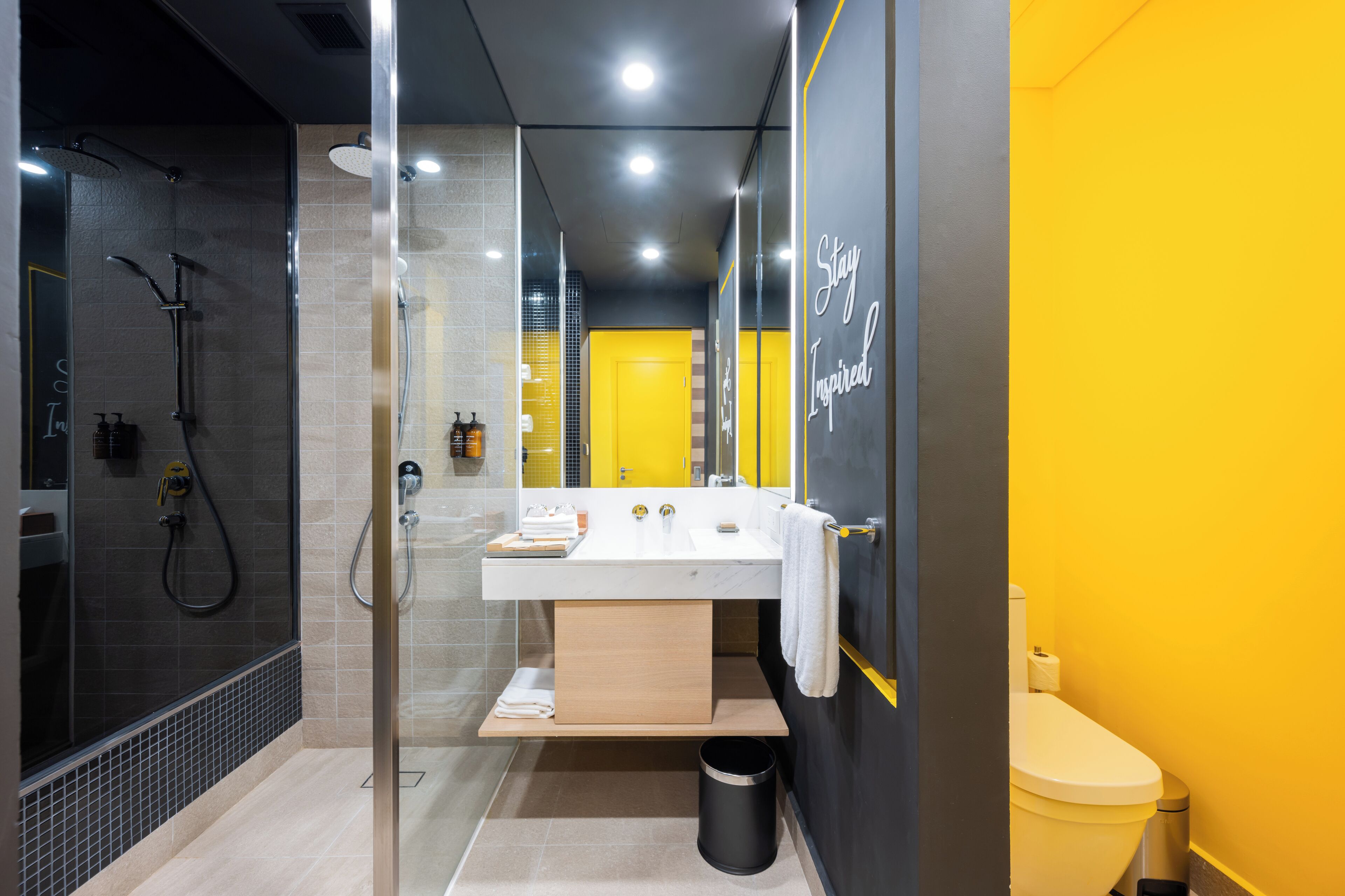 A modern bathroom with a glass-enclosed shower, a white sink, and a yellow accent wall.