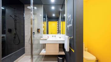 A modern bathroom with a glass-enclosed shower, a white sink, and a yellow accent wall.