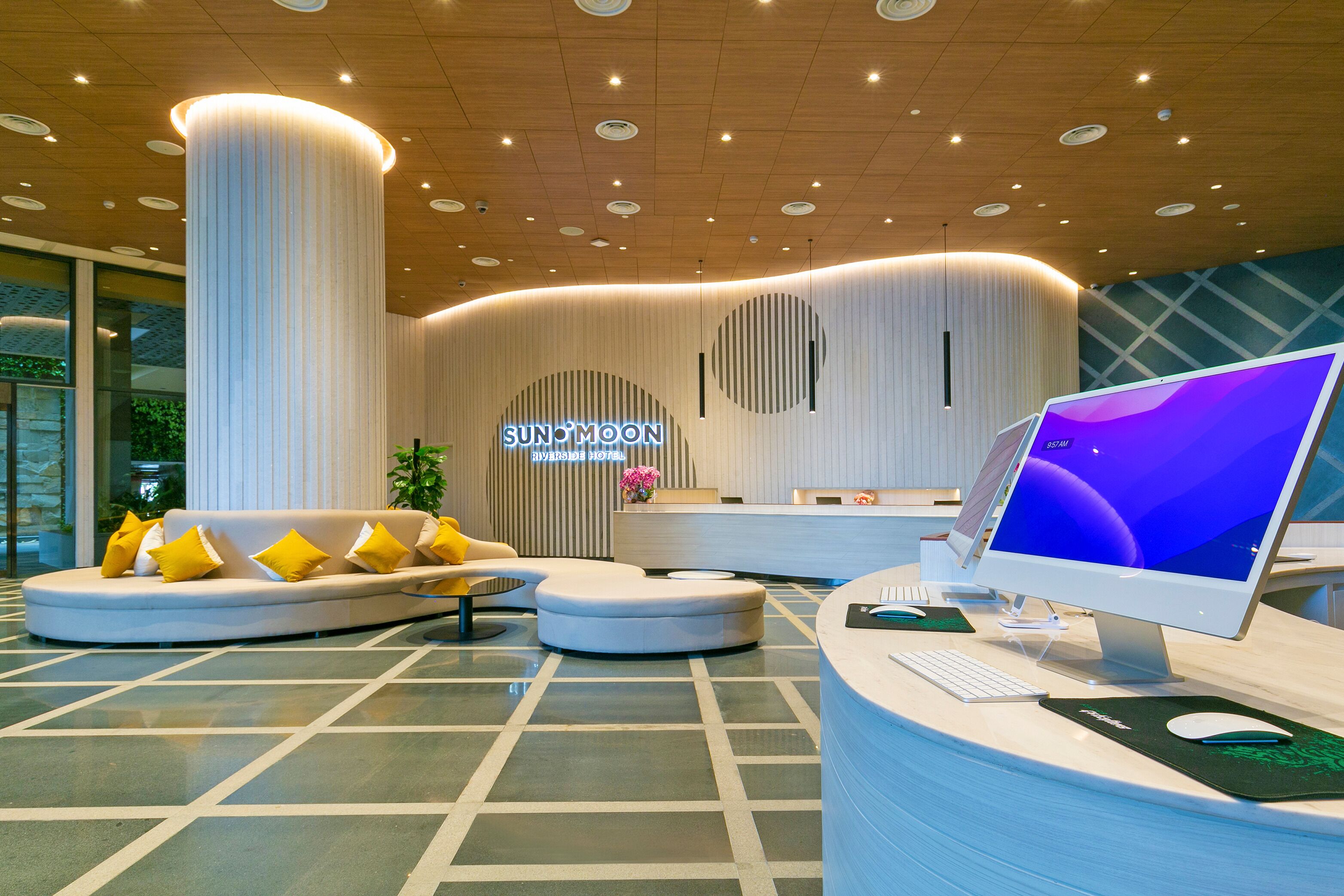 Et moderne hotelværelse med en buet receptionsdisk, en stor skærm og et loungeområde med sofa og stole.