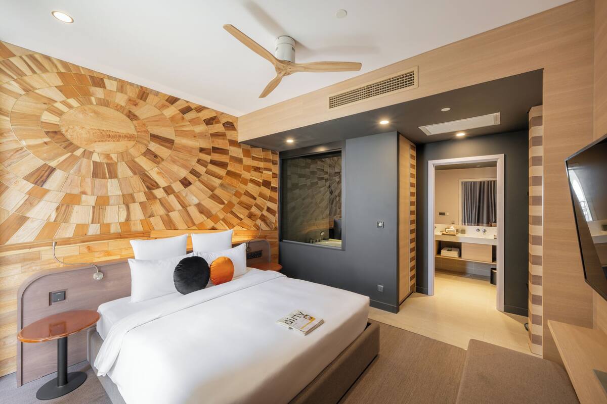 A modern hotel room with a wooden wall design, a bed with white bedding, a small table, and a ceiling fan.