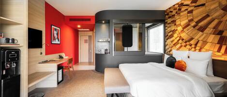 A modern hotel room with a bed, a desk, a coffee machine, and a TV.